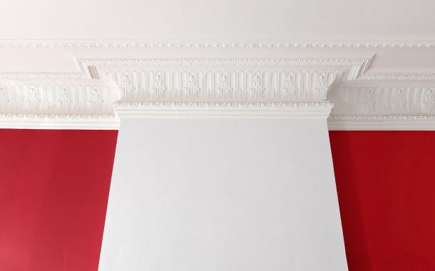 Renovierte Zimmerdecke einer Altbauwohnung mit eleganten Stuckverzierungen und roter Wand
