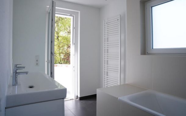 Bad in weiß saniert mit Badewanne und dunklen Fliesen.